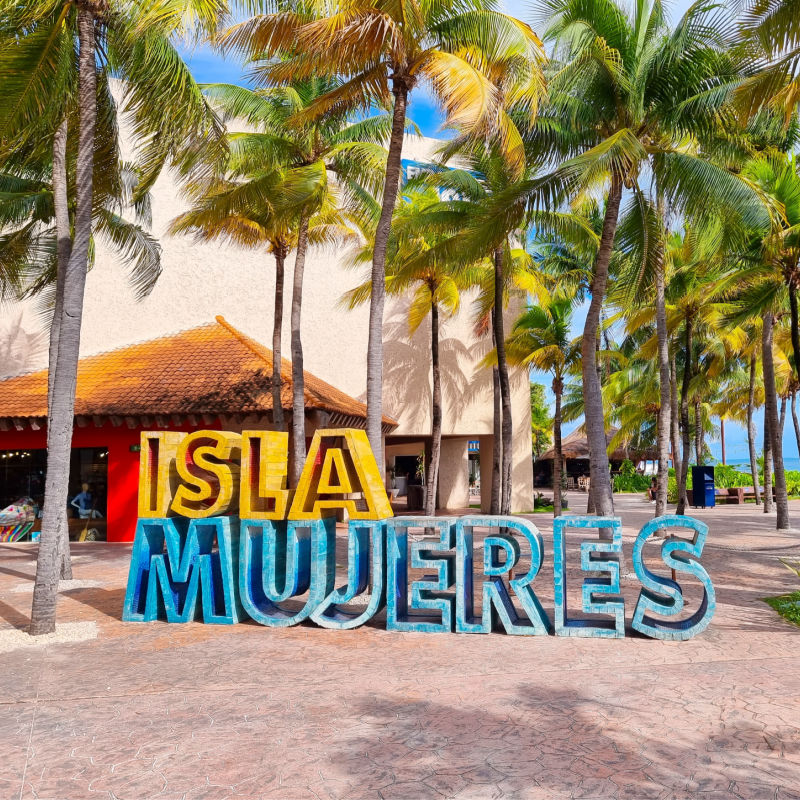 Cartel de Isla Mujeres en la playa rodeada de palmeras