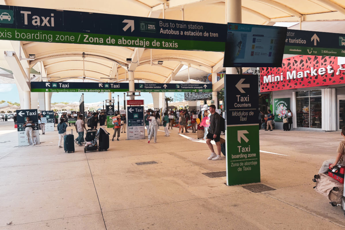 Área justo afuera de la terminal del aeropuerto de Cancún con minimercado y taxistas y camionetas esperando