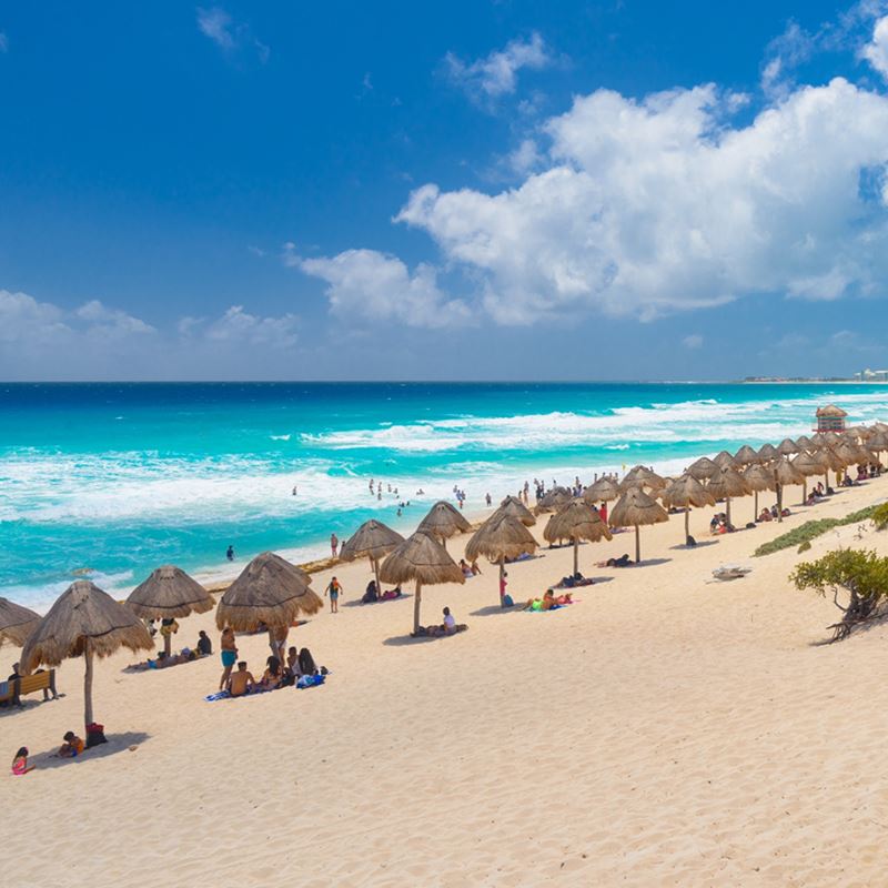 Playa de Cancún con palapas y turistas en un día soleado