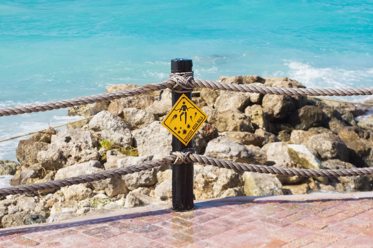 Señal de advertencia amarilla con medusas en un mar esmeralda Cancún México